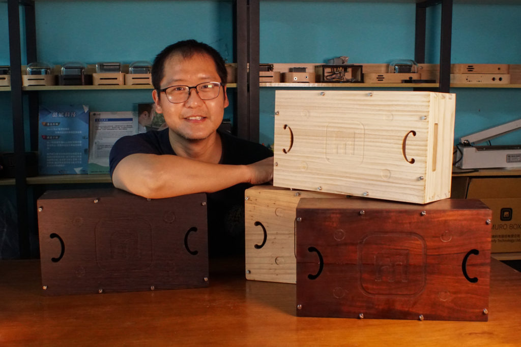 智慧音樂盒的發明人與他設計的四款原木共鳴箱，下排由左到右為雞翅木-日本柳杉-台灣相思木，上排(顏色較白)為松木。
