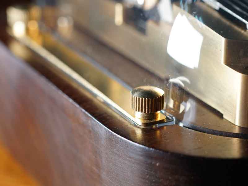 This is the acrylic top cover of the N40 Sublime model app-controlled and programmable music box. It can be removed by unscrewing the brass screws and lifting off the brass pressure strip. This convenient method allows for close-up viewing, photography, or touching the mechanism without opening the wooden case.