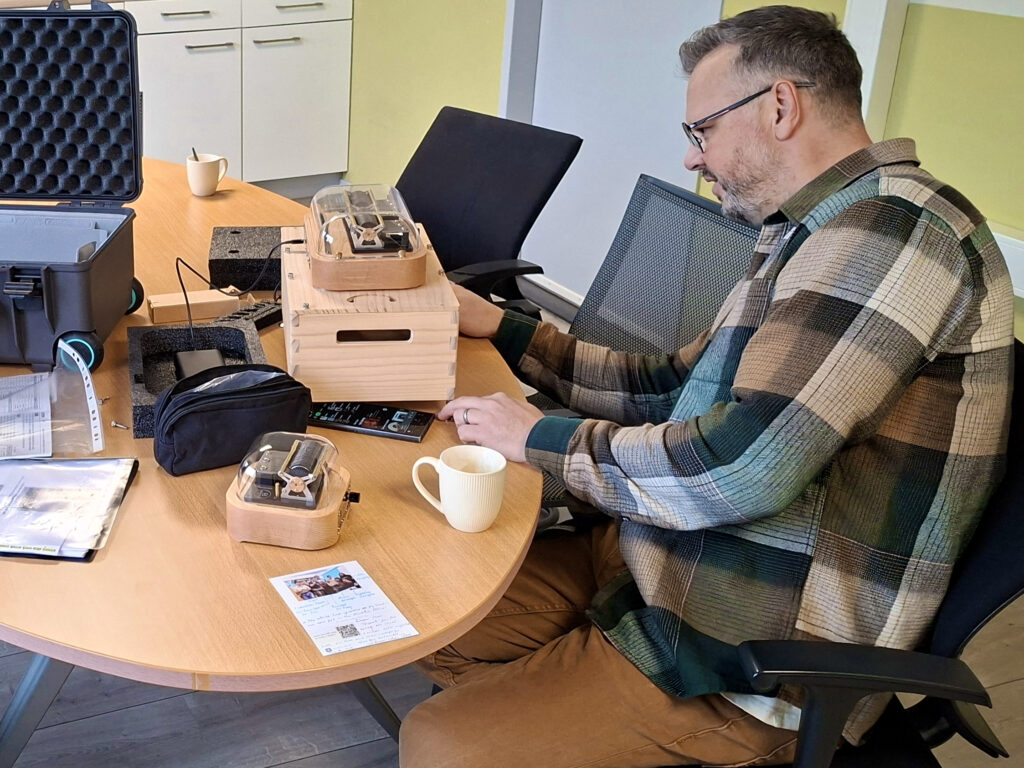 On an office desk, there are two Muro Box smart music boxes. A man wearing glasses is carefully examining the larger one — the Muro Box-N40 Standard Edition.